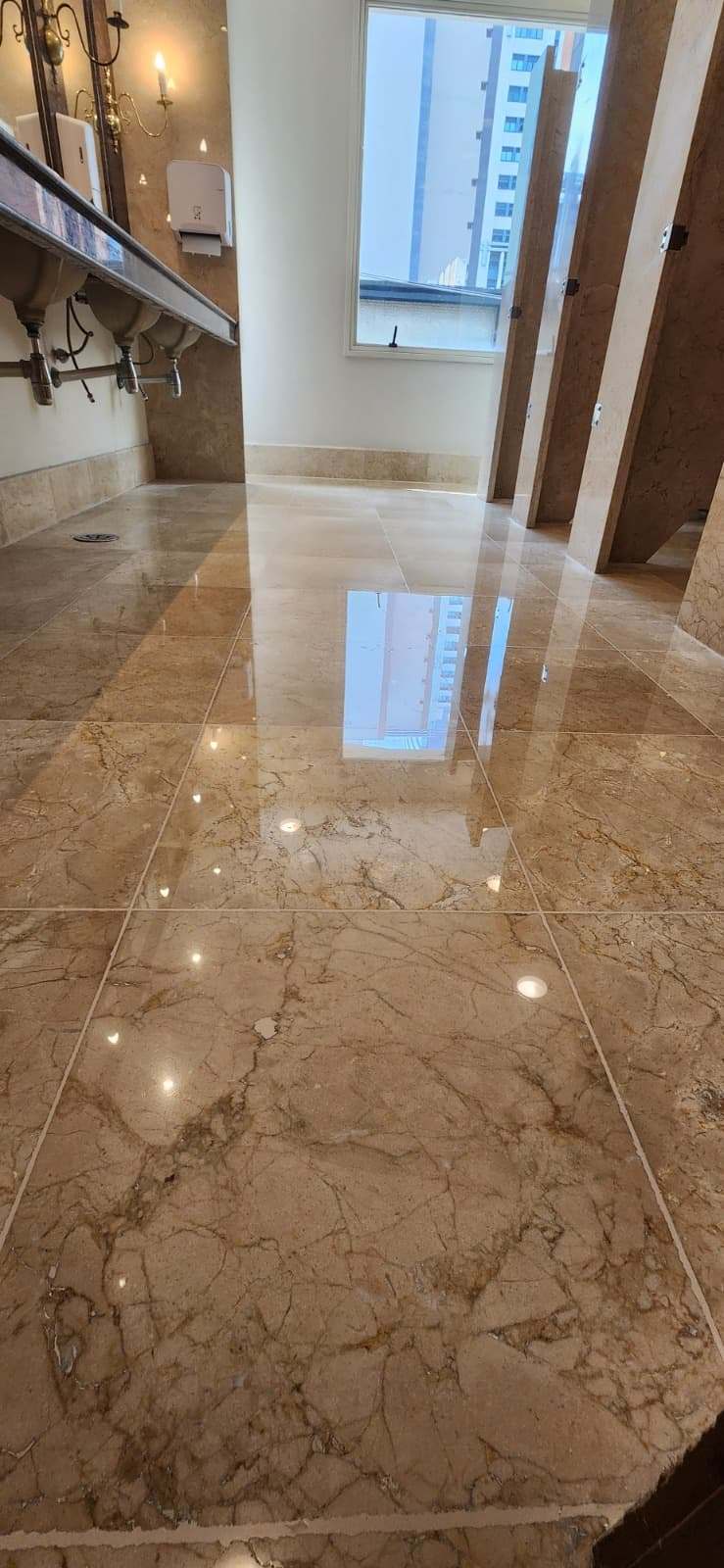 Banheiro corporativo com piso de mármore polido refletindo a luz natural
